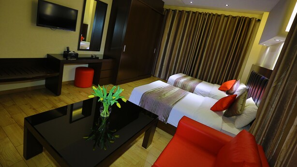 A hotel room with a bed, a sofa, a TV, a desk, and a mirror. - Jounieh Suites Hotel (Jounieh)