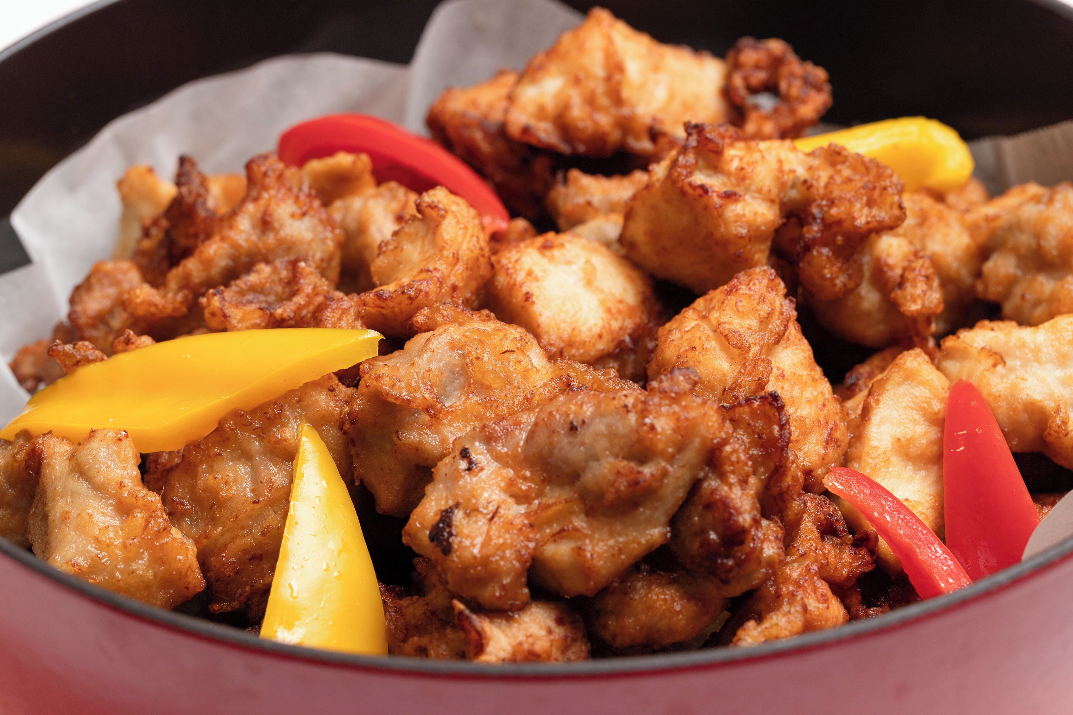 A bowl of fried chicken with yellow and red bell peppers.