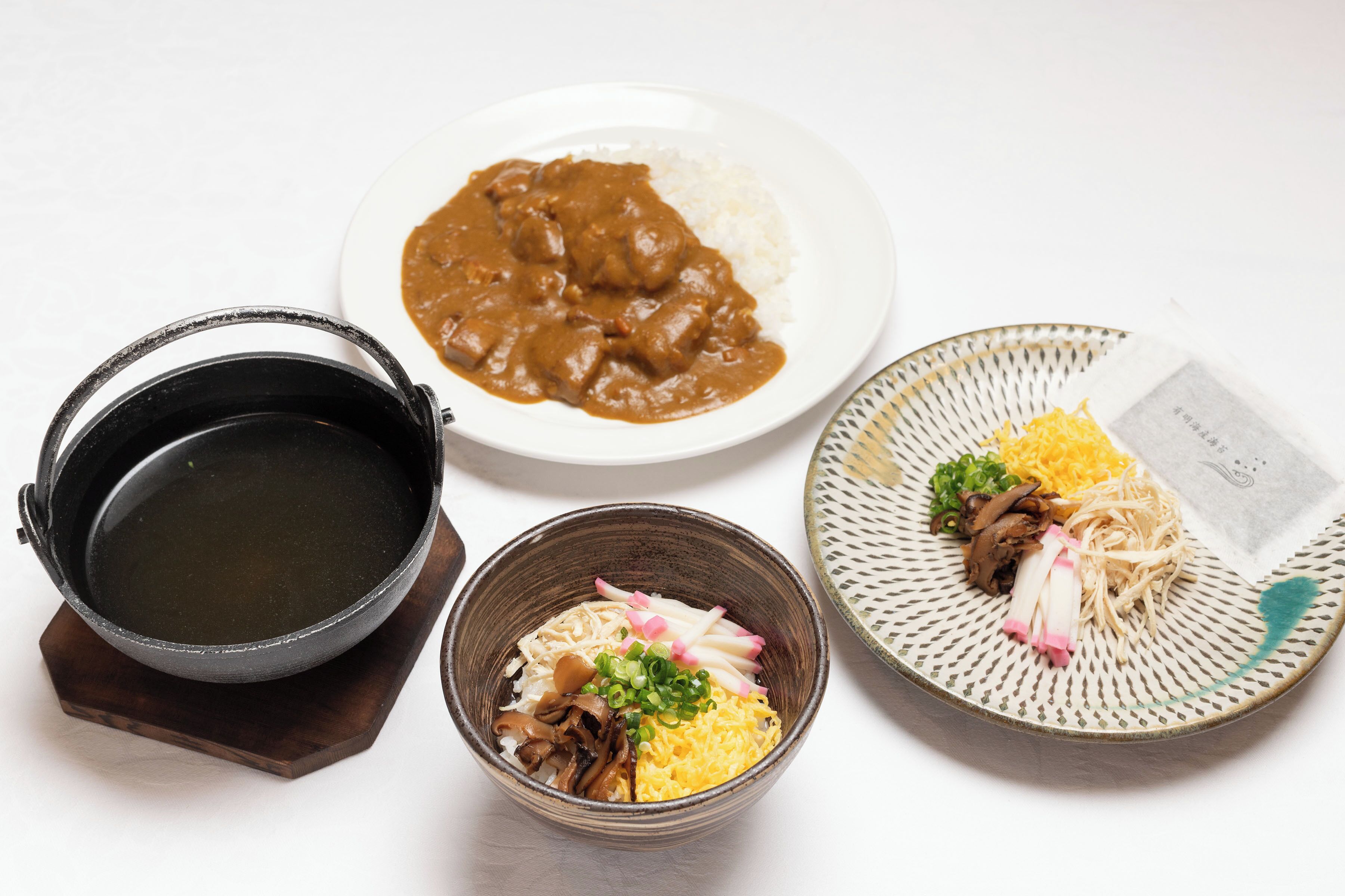 A variety of dishes including a bowl of soup, a plate of rice with curry, and a plate with noodles and vegetables.