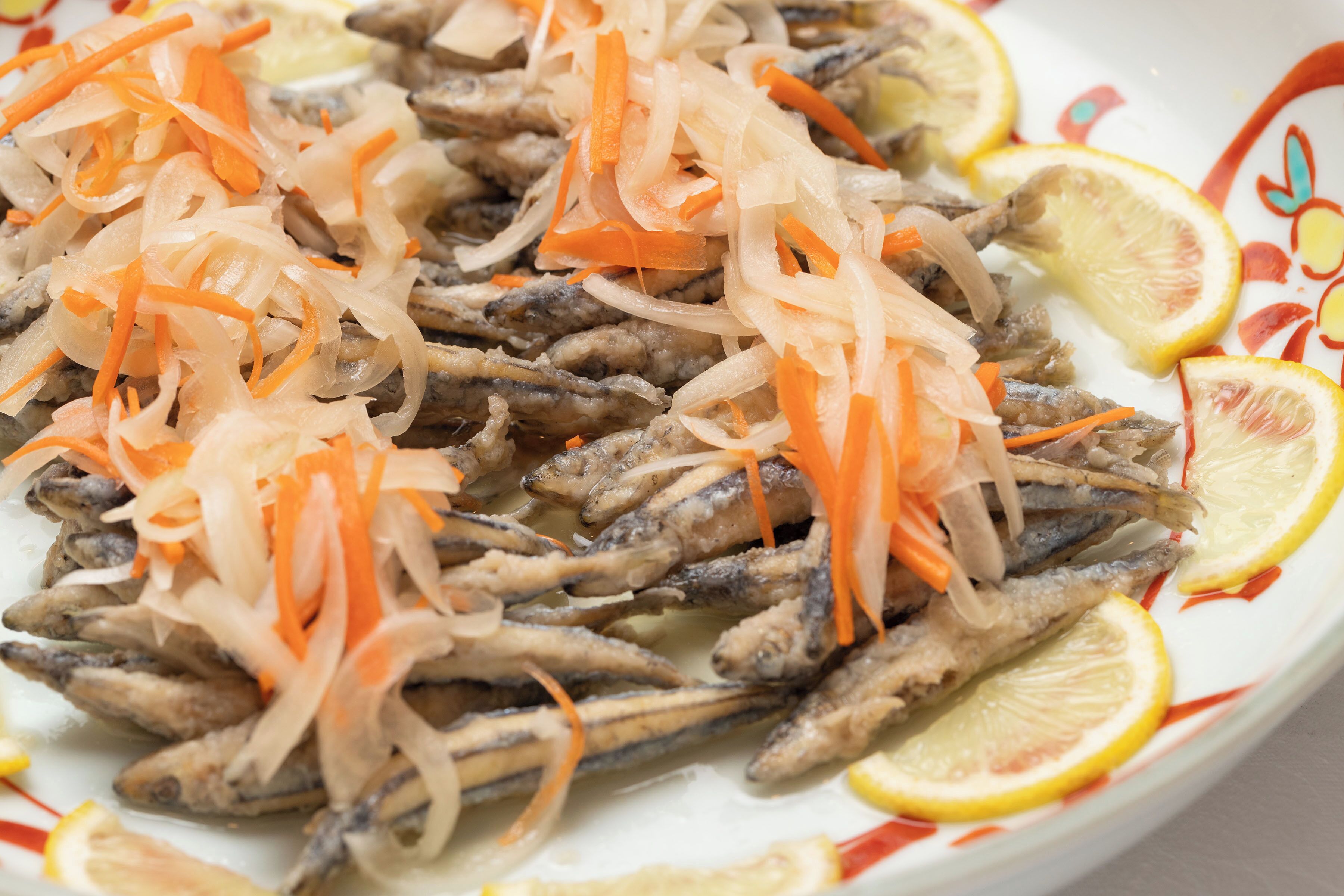 A plate of fish with shredded carrots and lemon slices.