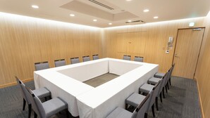 Un salón de conferencias con una gran mesa rectangular, sillas tapizadas en gris y suelo alfombrado.