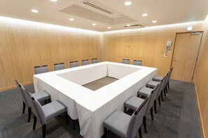Un salón de conferencias con una gran mesa rectangular, sillas tapizadas en gris y suelo alfombrado.