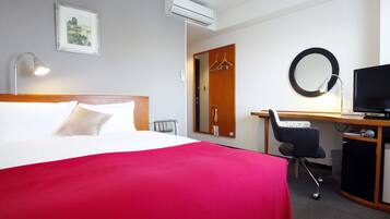 Habitación de hotel con cama, escritorio, silla, televisor y espejo.