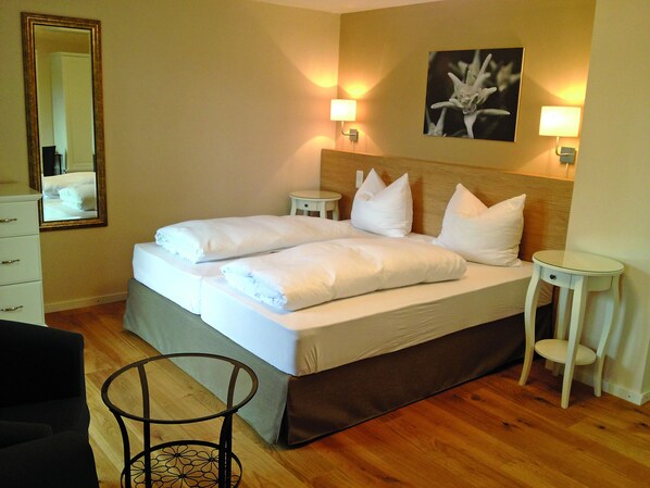 A double bed with white linens and pillows, two bedside tables, a small round table, a mirror, and a wall-mounted picture. - Alpenhof Landhotel Restaurant (Oberaudorf)