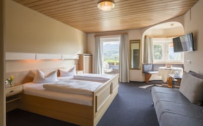 Ein Hotelzimmer mit einem großen Bett, einem Sofa, einem Fernseher und einem Fenster mit Blick ins Freie.