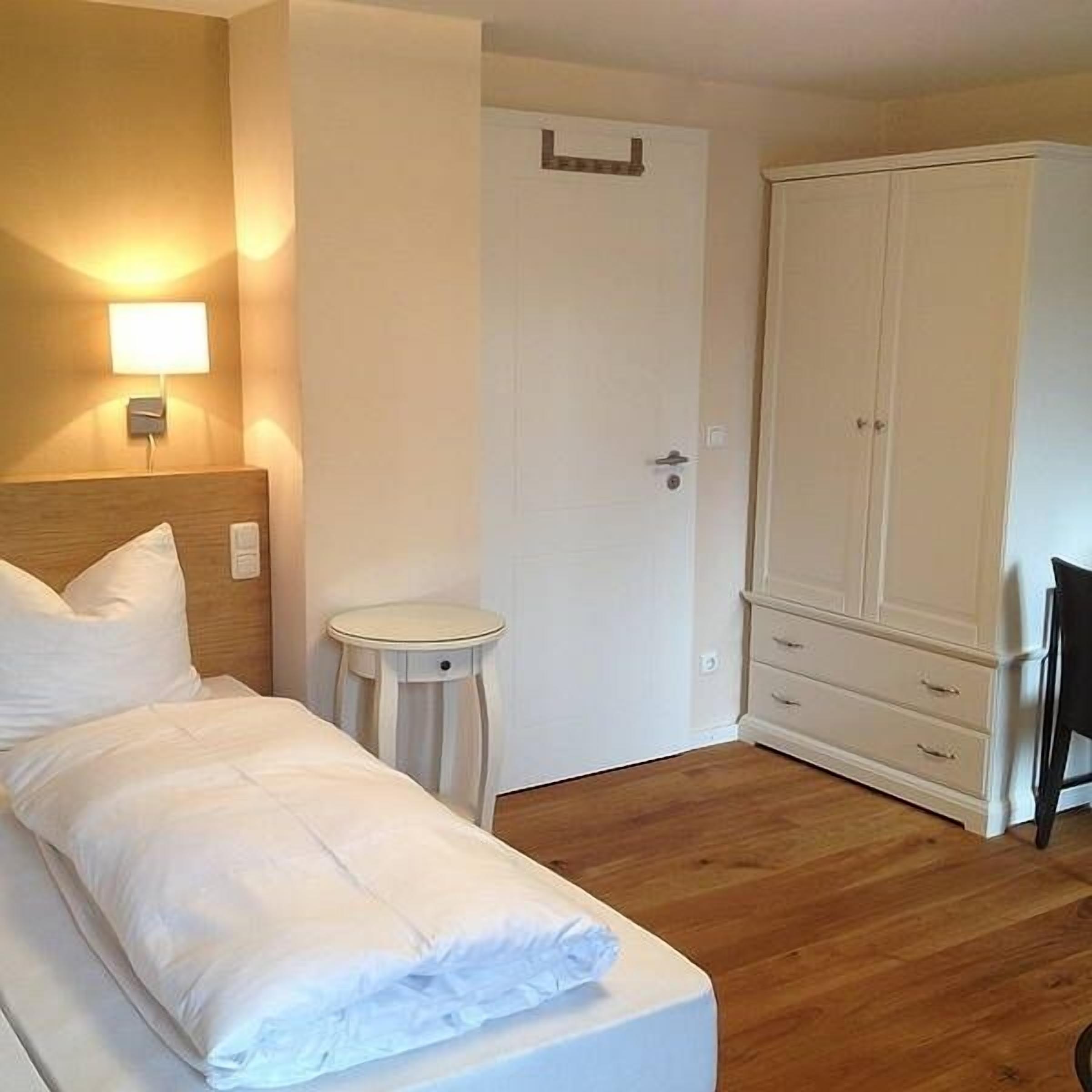 Een hotelkamer met een bed, nachtkastje, kledingkast en een wandlamp.
