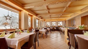 A restaurant with wooden ceiling and walls, large windows with curtains, and tables set for dining. - Alpenhof Landhotel Restaurant (Oberaudorf)