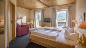 A hotel room with a bed, a desk, a TV, and a balcony with a view of the mountains. - Alpenhof Landhotel Restaurant (Oberaudorf)