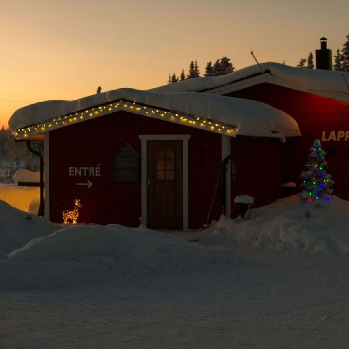 Un edificio rojo con un letrero que dice "ENTRÉE" y un árbol de Navidad con luces.