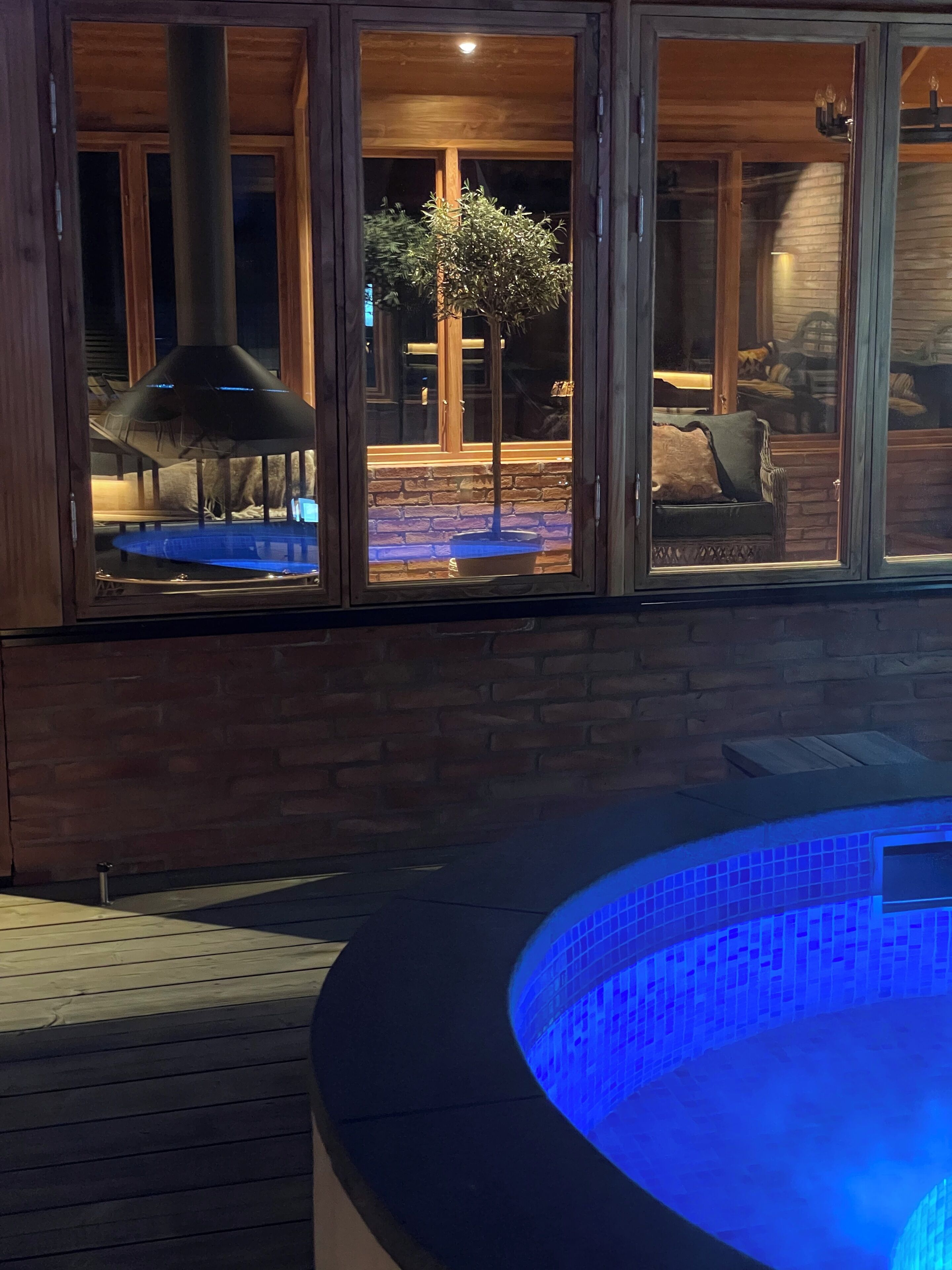 Ein Whirlpool mit blauem Licht, eine Holzterrasse und eine Ziegelwand.