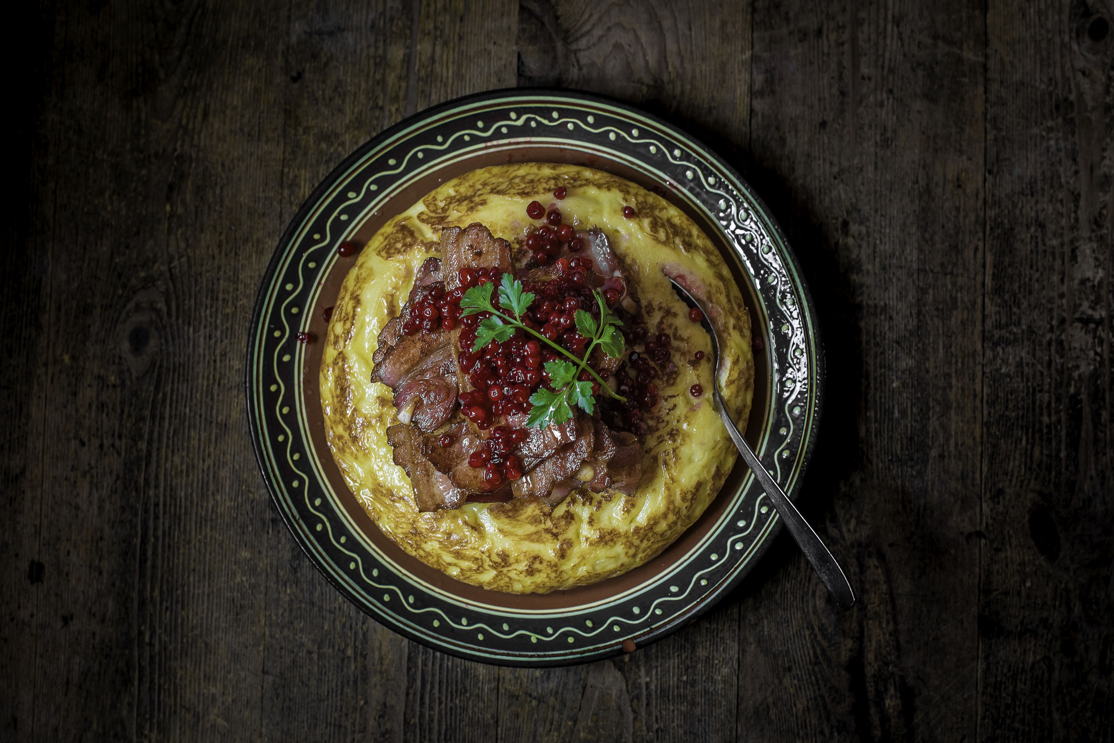 A plate of food with meat and berries on a dark wooden table.