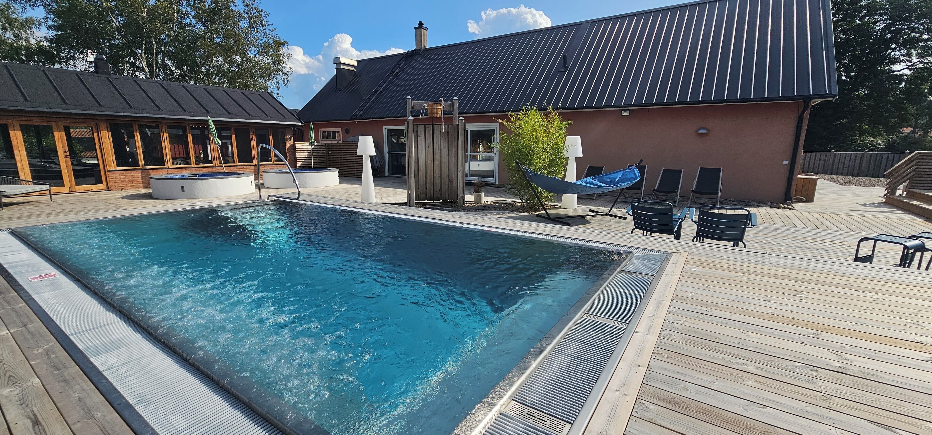 Ein Schwimmbecken mit Holzterrasse, Liegestühlen und einem Whirlpool.