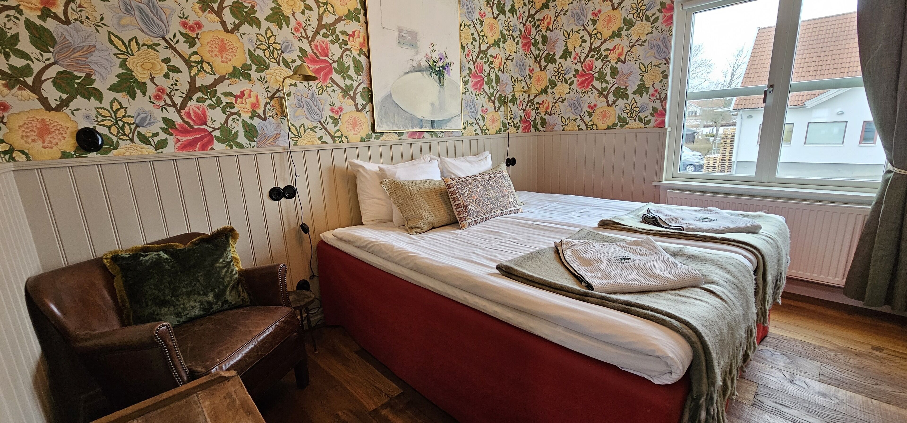 A bedroom with a bed, pillows, a bench, and a floral wallpaper.