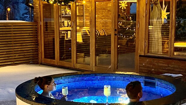 A hot tub in a snowy outdoor setting with a wooden deck and glass doors. - Brösarps Gästgifveri & SPA (Brosarp)