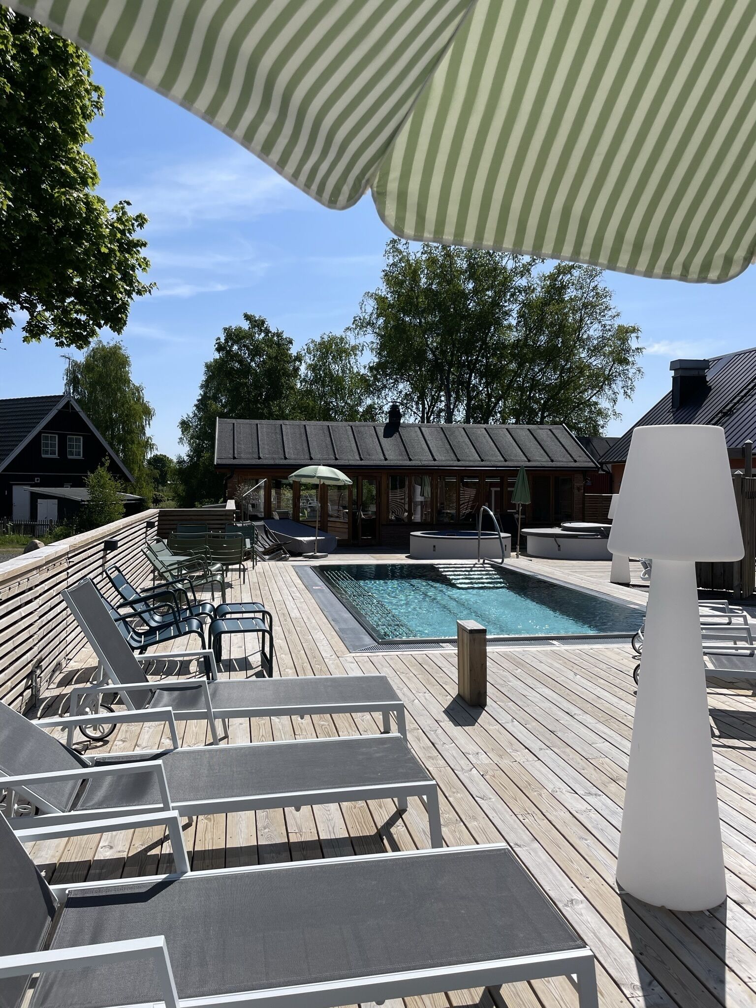 A wooden deck with a pool, lounge chairs, and a covered seating area.