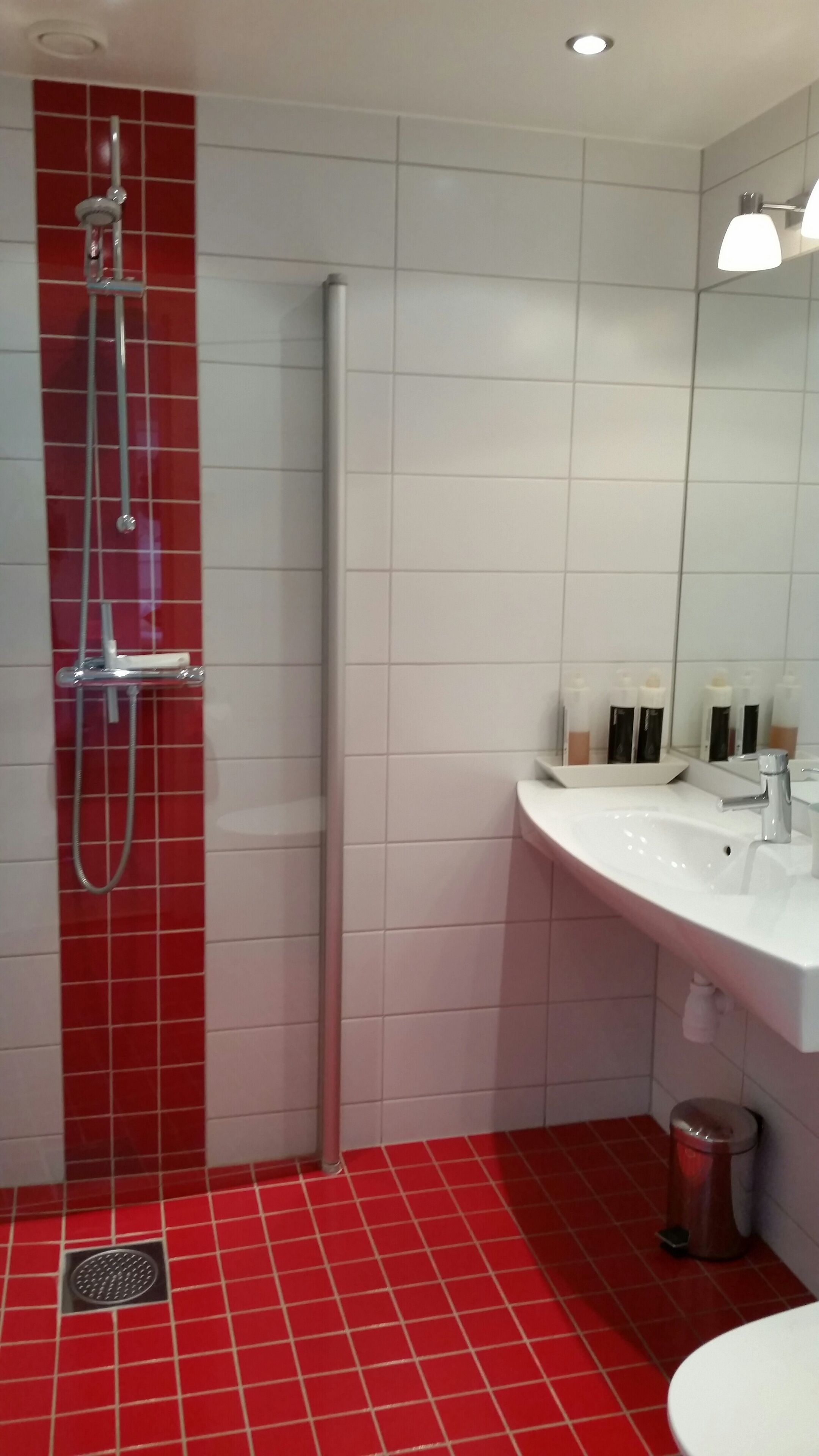 Une salle de bain moderne avec une douche dont le carrelage est rouge, un lavabo blanc et un miroir au-dessus du lavabo.