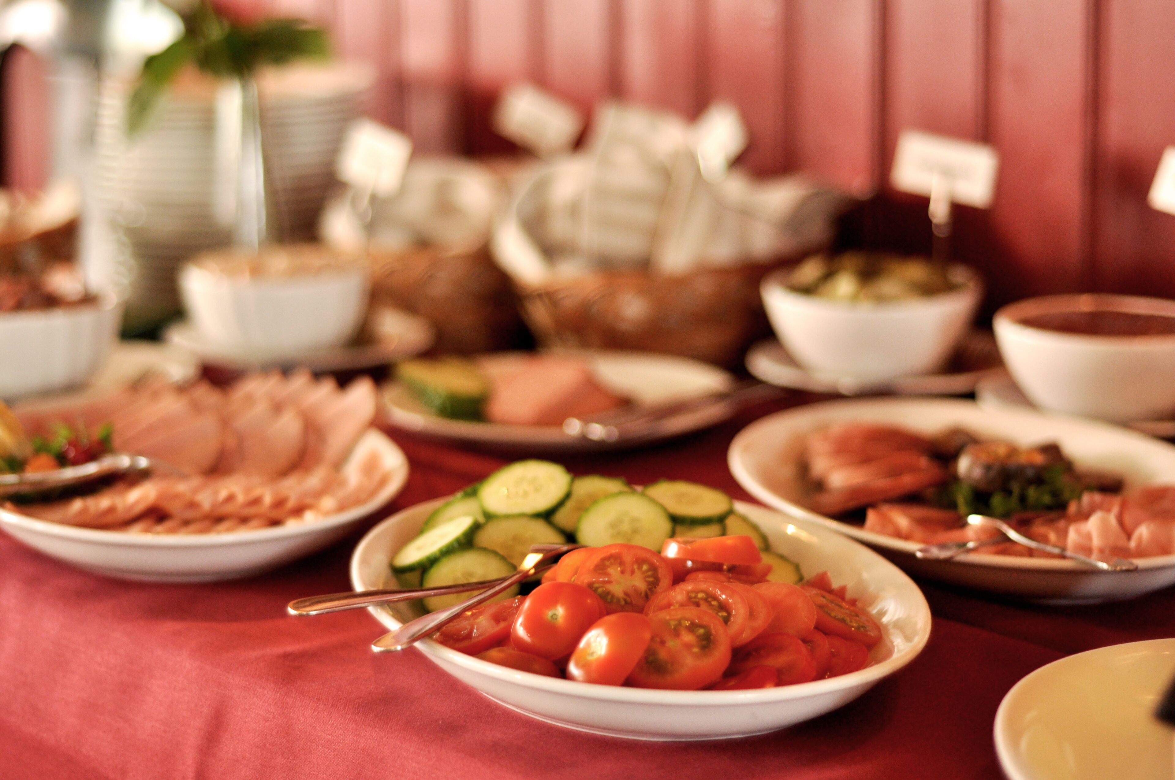 A buffet table with various dishes including sliced cucumbers, tomatoes, and meats.
