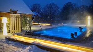 A heated outdoor swimming pool surrounded by snow, with a wooden deck and a lamp post. - Brösarps Gästgifveri & SPA (Brosarp)