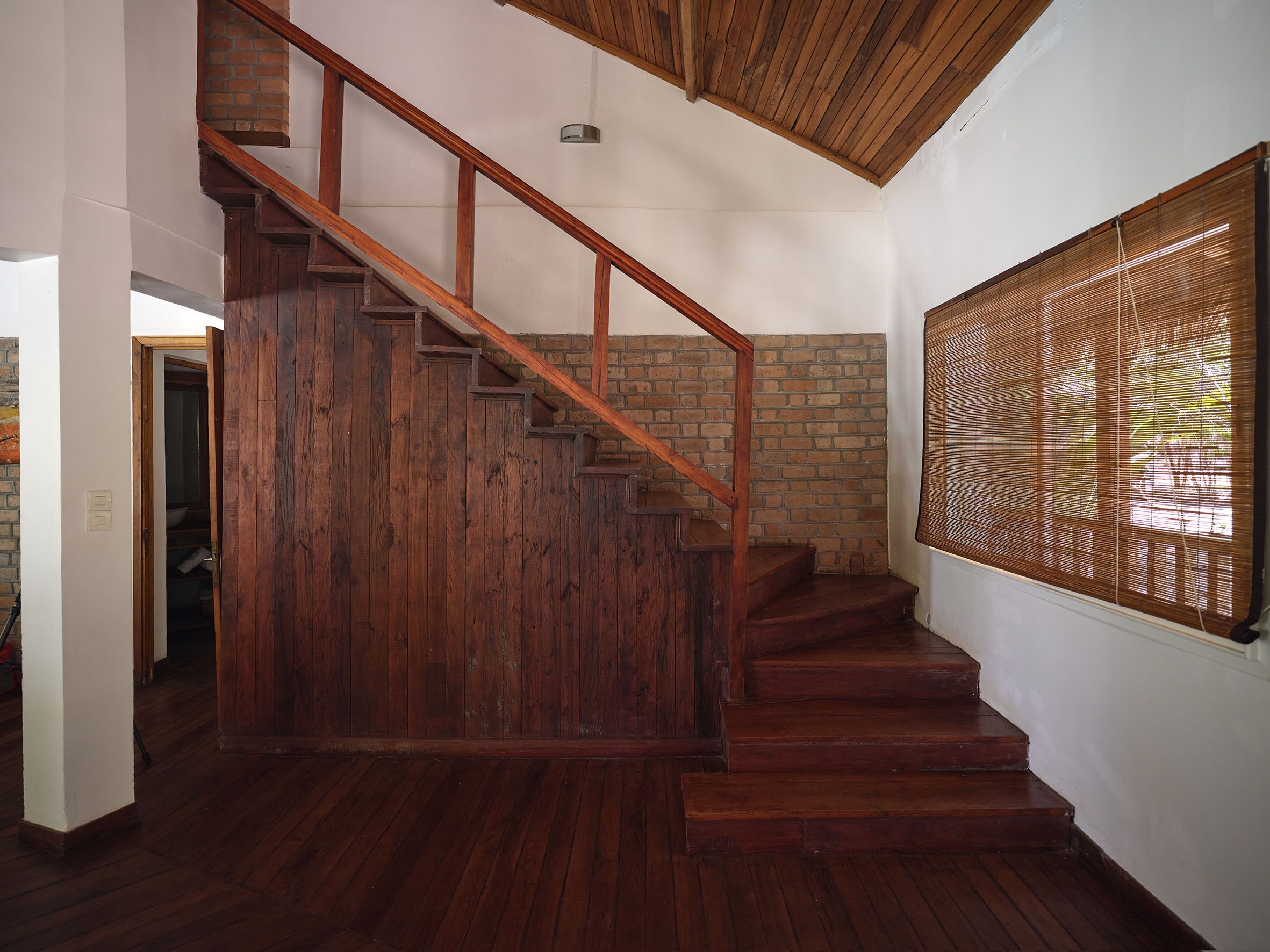 A wooden staircase with a brick wall and a window with bamboo blinds.