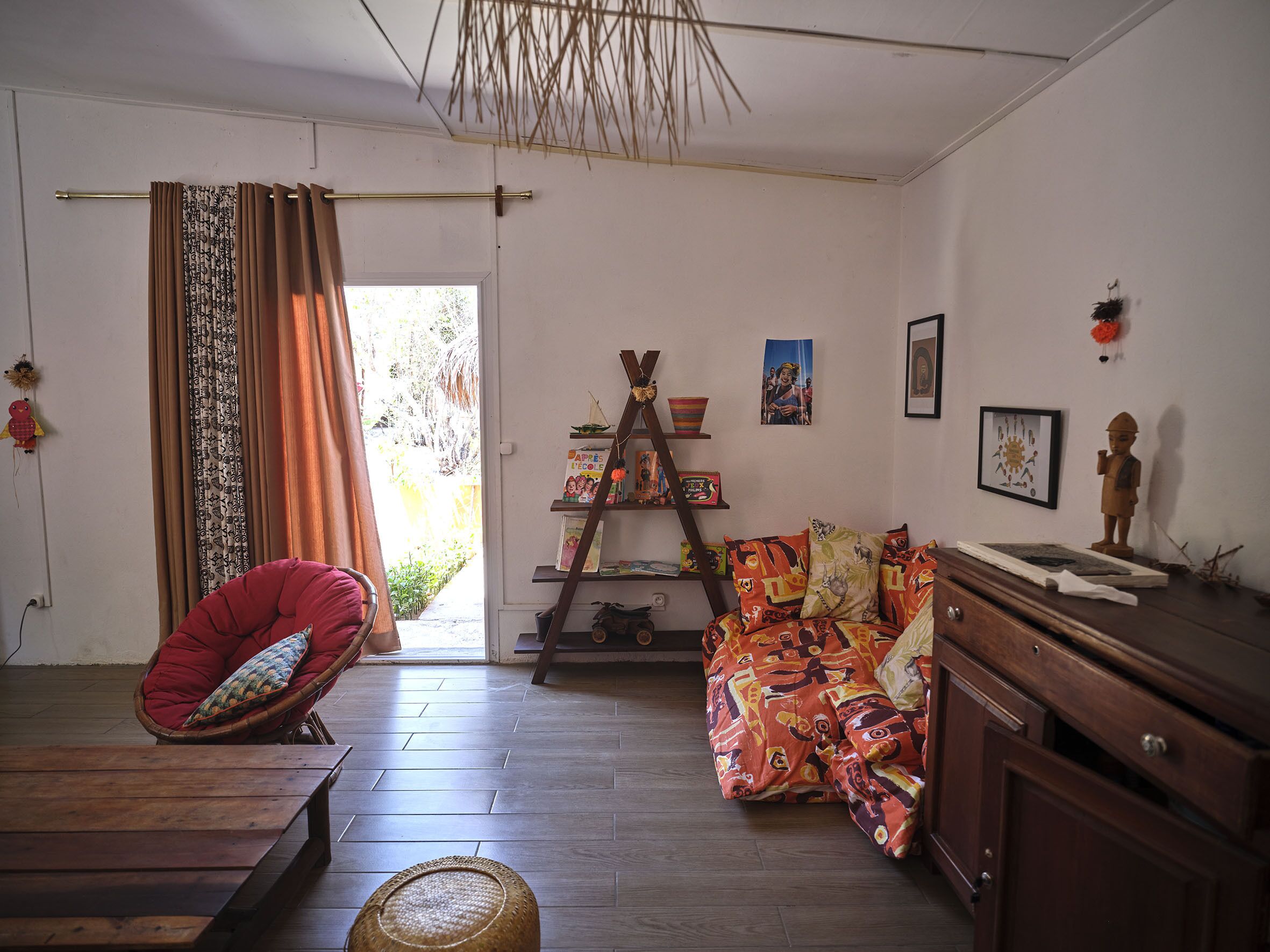 A cozy living room with a wooden floor, a red chair, a colorful sofa, and a wooden cabinet.