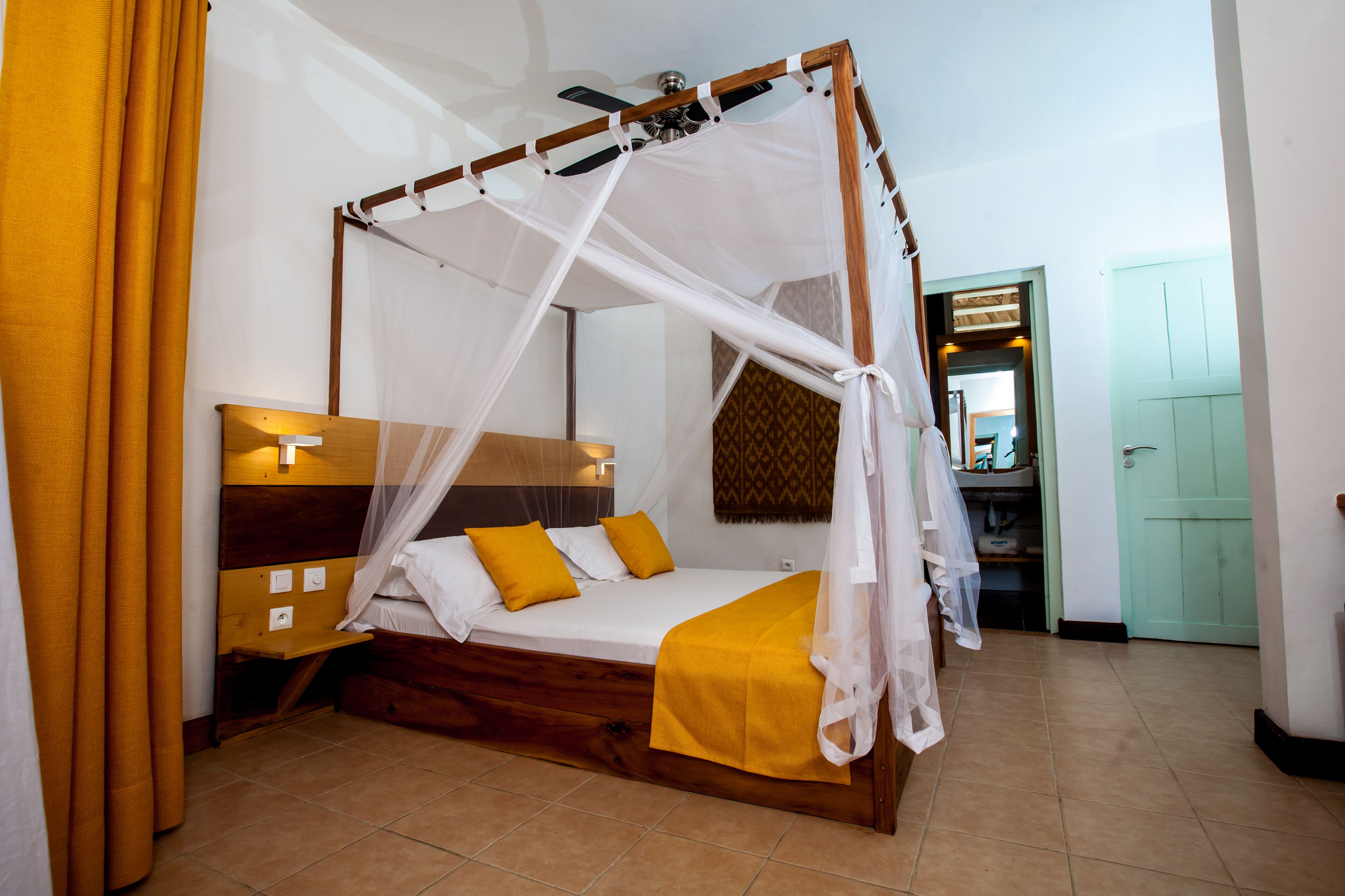 Una habitación con una cama de madera con dosel, una mesita de noche y un velador.