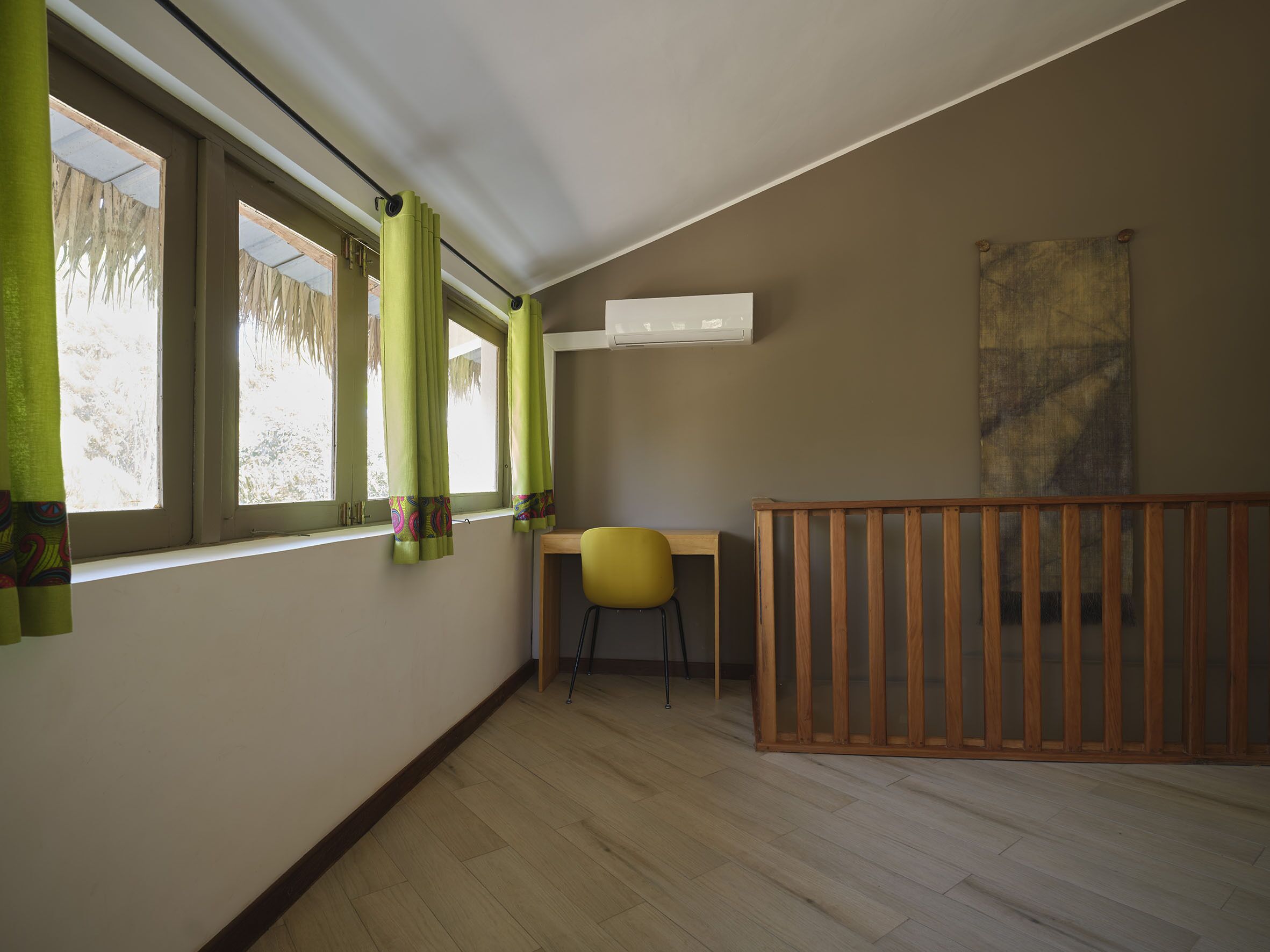 Une pièce avec un plancher en bois, une chaise jaune, un berceau en bois et une fenêtre ornée de rideaux verts.