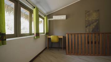 Une pièce avec un plancher en bois, une chaise jaune, un berceau en bois et une fenêtre ornée de rideaux verts.