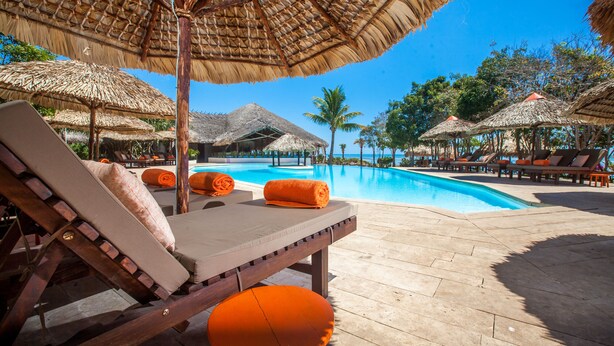 Een zwembadterras met ligbedden en rieten parasols.