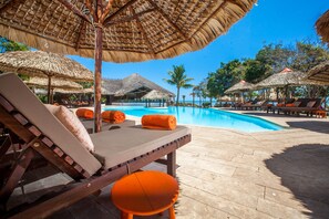 Un área junto a la piscina con sillones de descanso y sombrillas de paja.