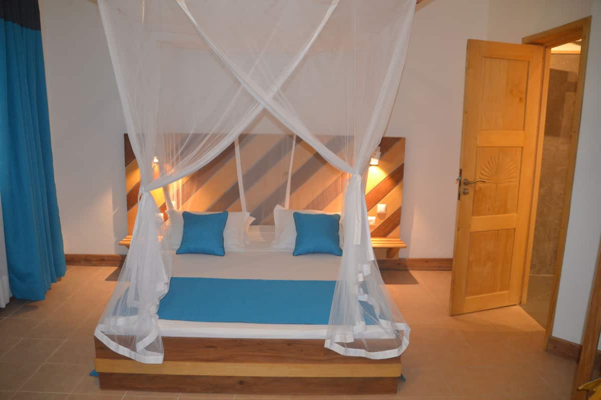 Un dormitorio con cama bajo dosel, una puerta de madera y una lámpara fijada a la pared.