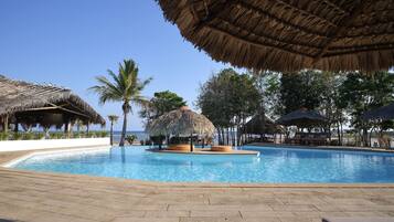 Relax by the ocean with a clear view from this resort's pool area, surrounded by a paved deck and shaded by thatched-roof structures.