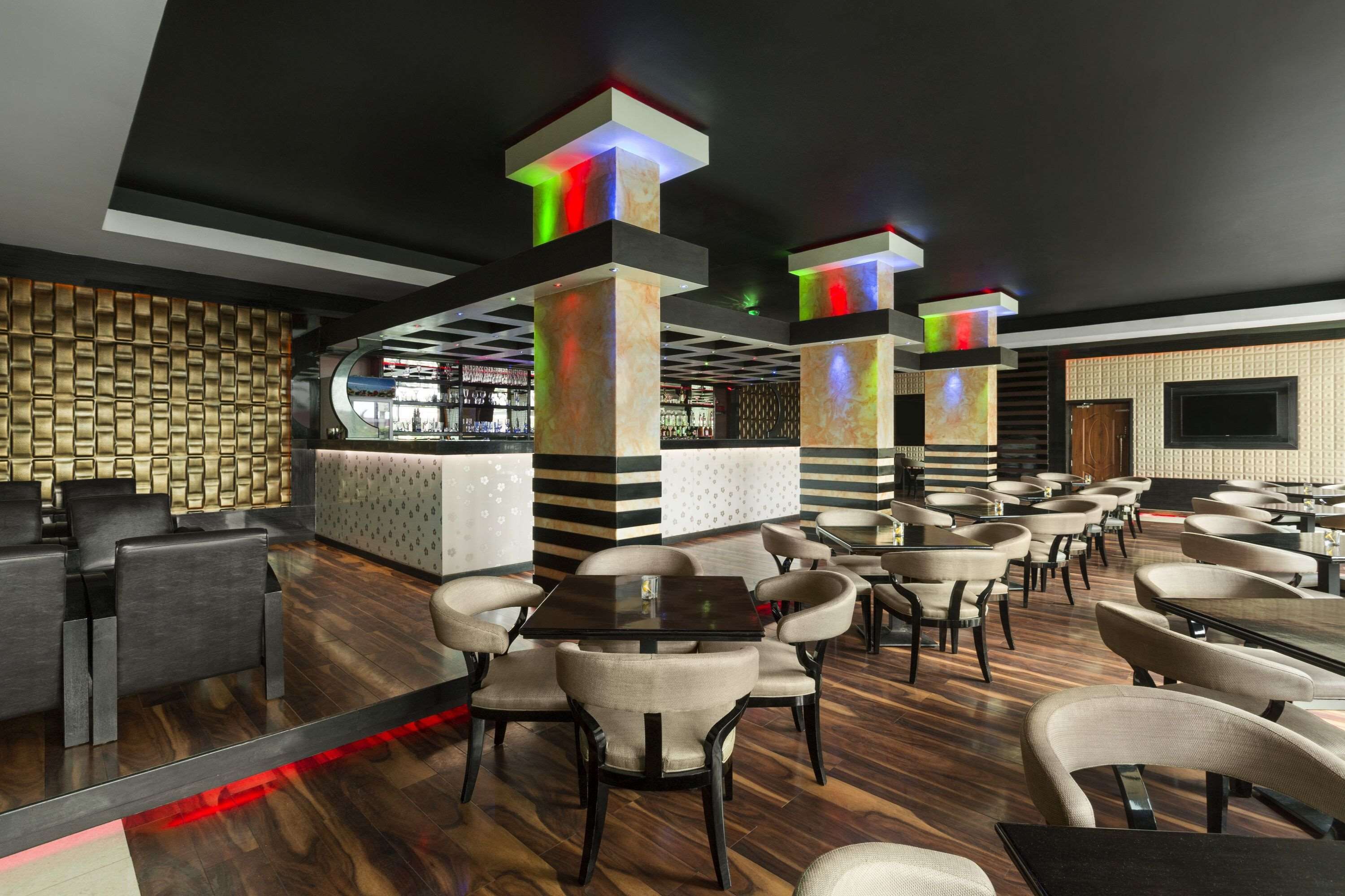 A modern restaurant with wooden flooring, black and white patterned walls, and multiple seating areas including tables and chairs.
