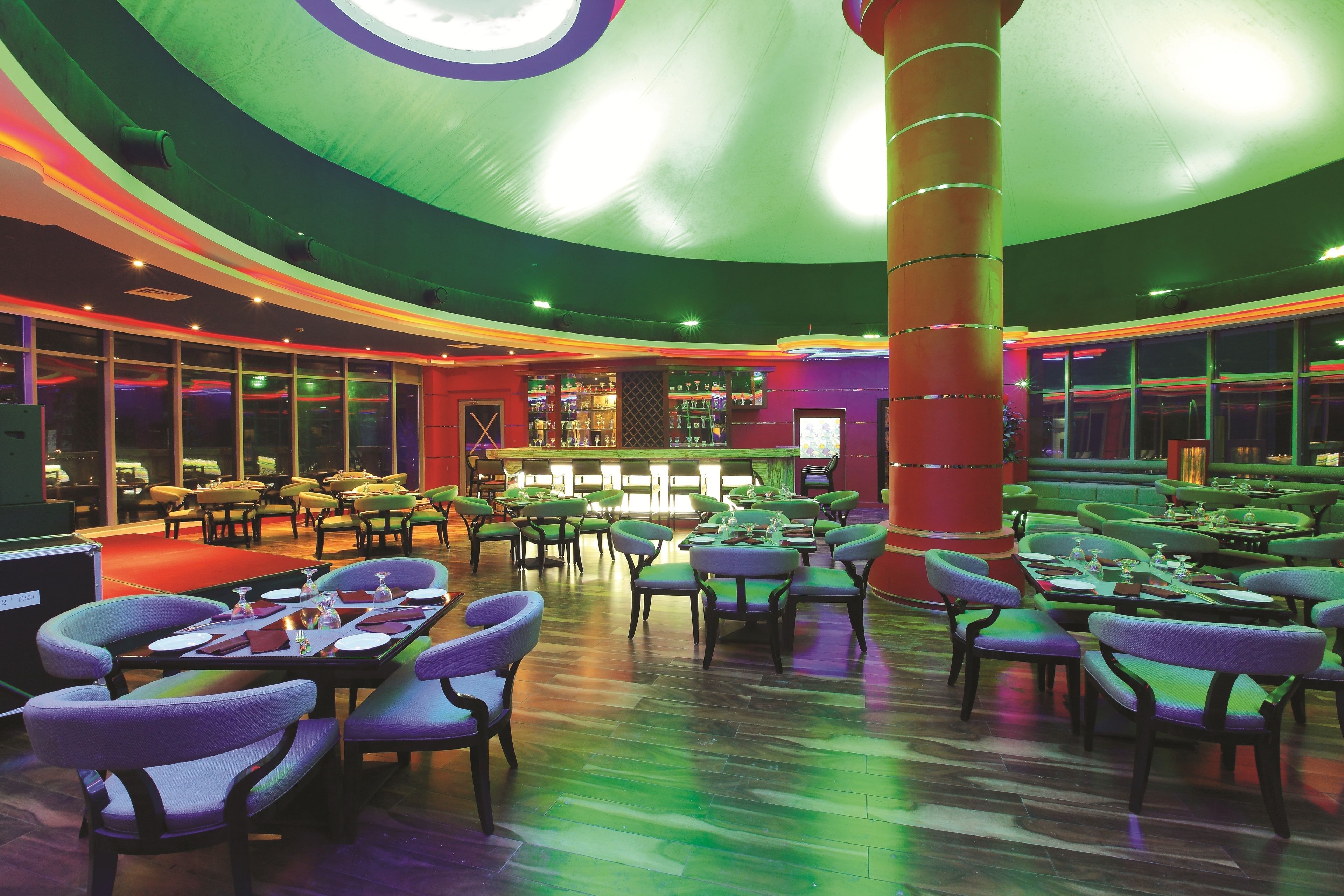 Een ruime binnenruimte met diverse zithoeken, een centrale pilaar en een bar met flessen op de planken.