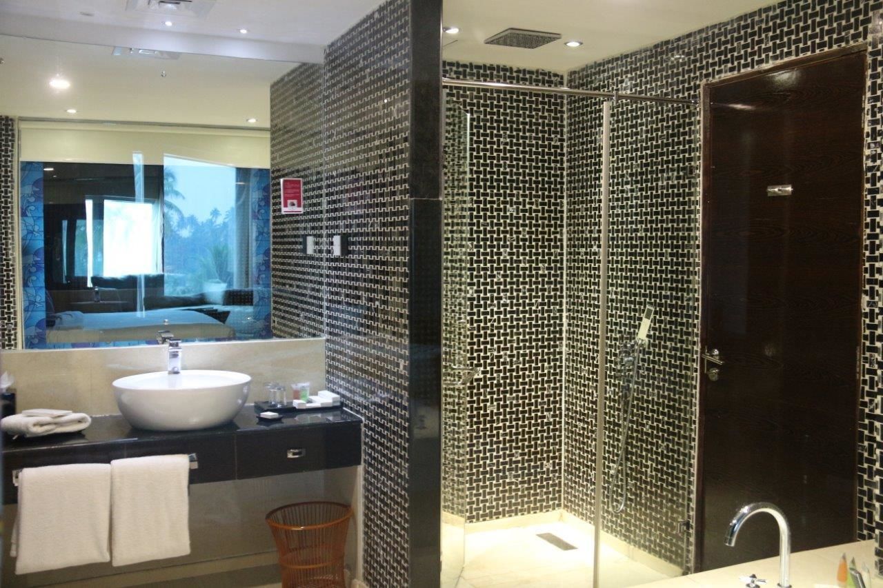 Un baño moderno con un espejo grande, un lavamanos redondo y una zona de ducha con pared de azulejos.