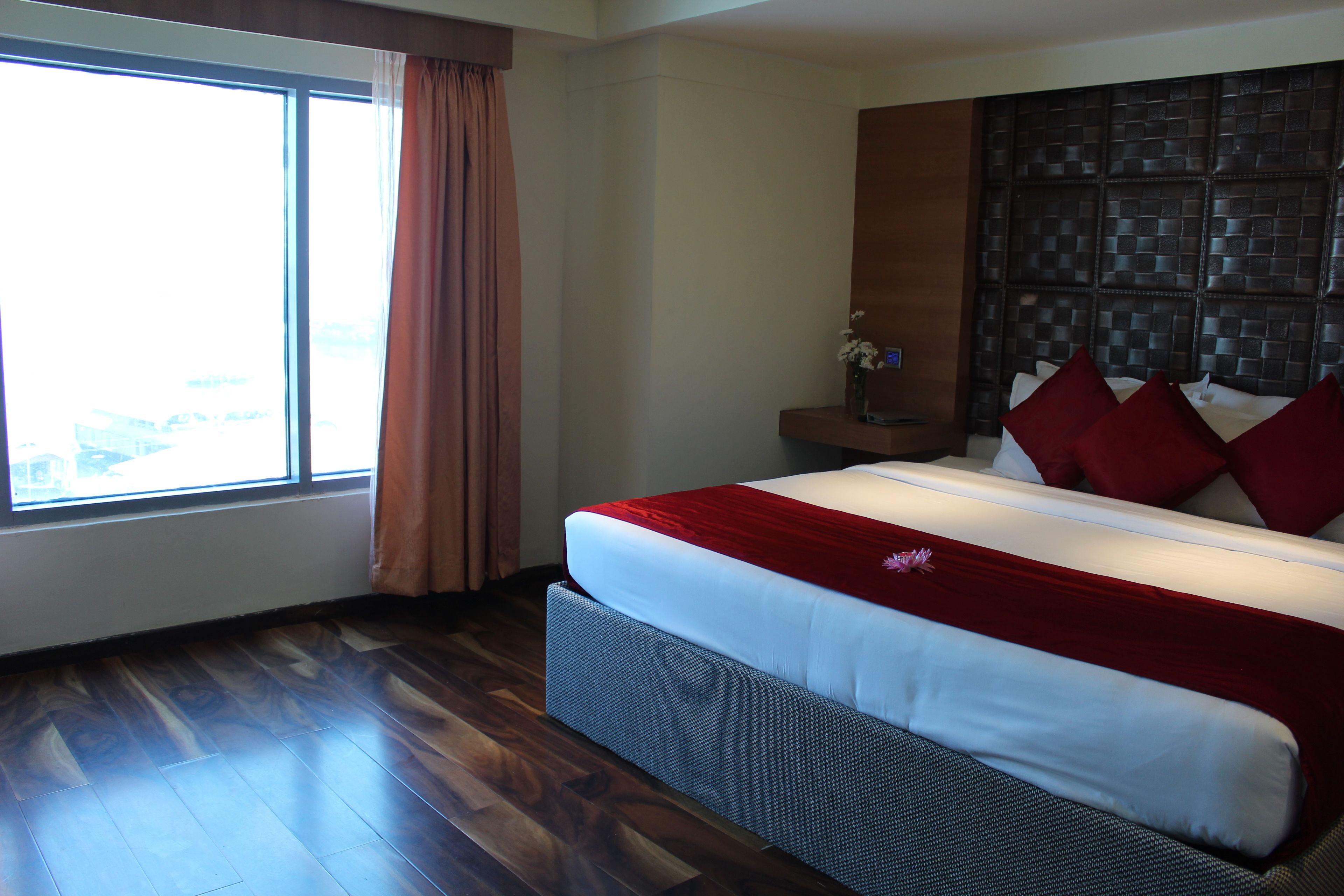 A hotel room with a large bed, a wooden floor, a window with curtains, and a decorative wall panel.