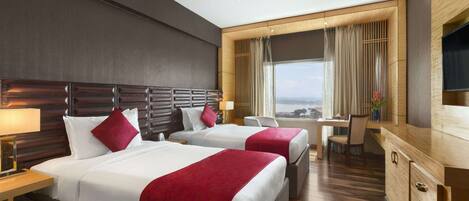 A hotel room with two beds, a desk, and a large window with curtains.