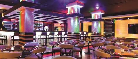A restaurant with multiple tables and chairs, illuminated by colorful ceiling lights.