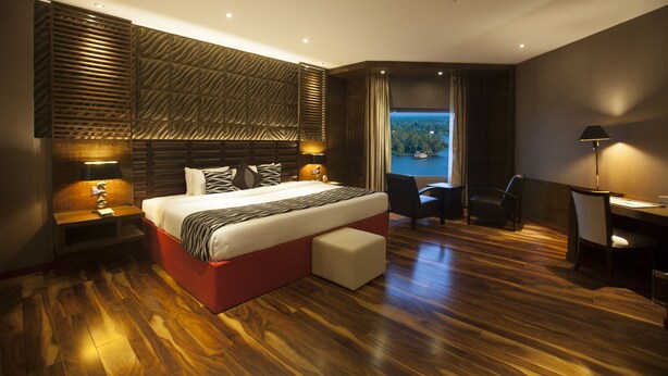 A modern hotel room with a large bed, a desk, and a view of the outdoors. - Ramada by Wyndham Alleppey (Ambalapuzha)