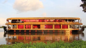 A double-deck riverboat with multiple lifebuoys, red curtains, and a reflection on the water. - Ramada by Wyndham Alleppey (Ambalapuzha)