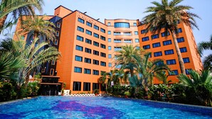A modern hotel with a large swimming pool surrounded by palm trees and lush greenery. - Ramada by Wyndham Alleppey (Ambalapuzha)