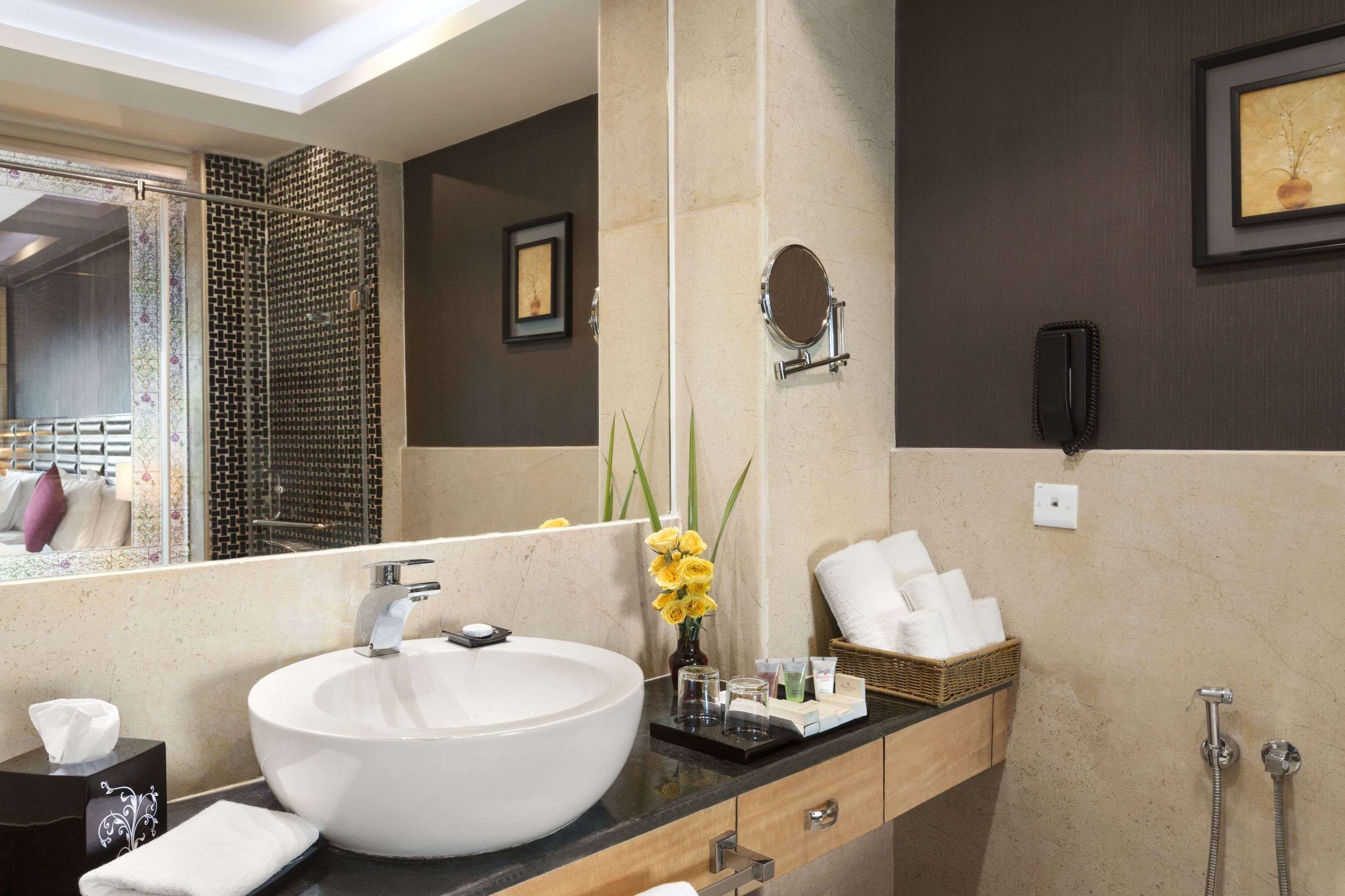Un baño moderno con un lavamanos grande de color blanco, un espejo, un cuadro enmarcado, un teléfono y una zona de ducha.
