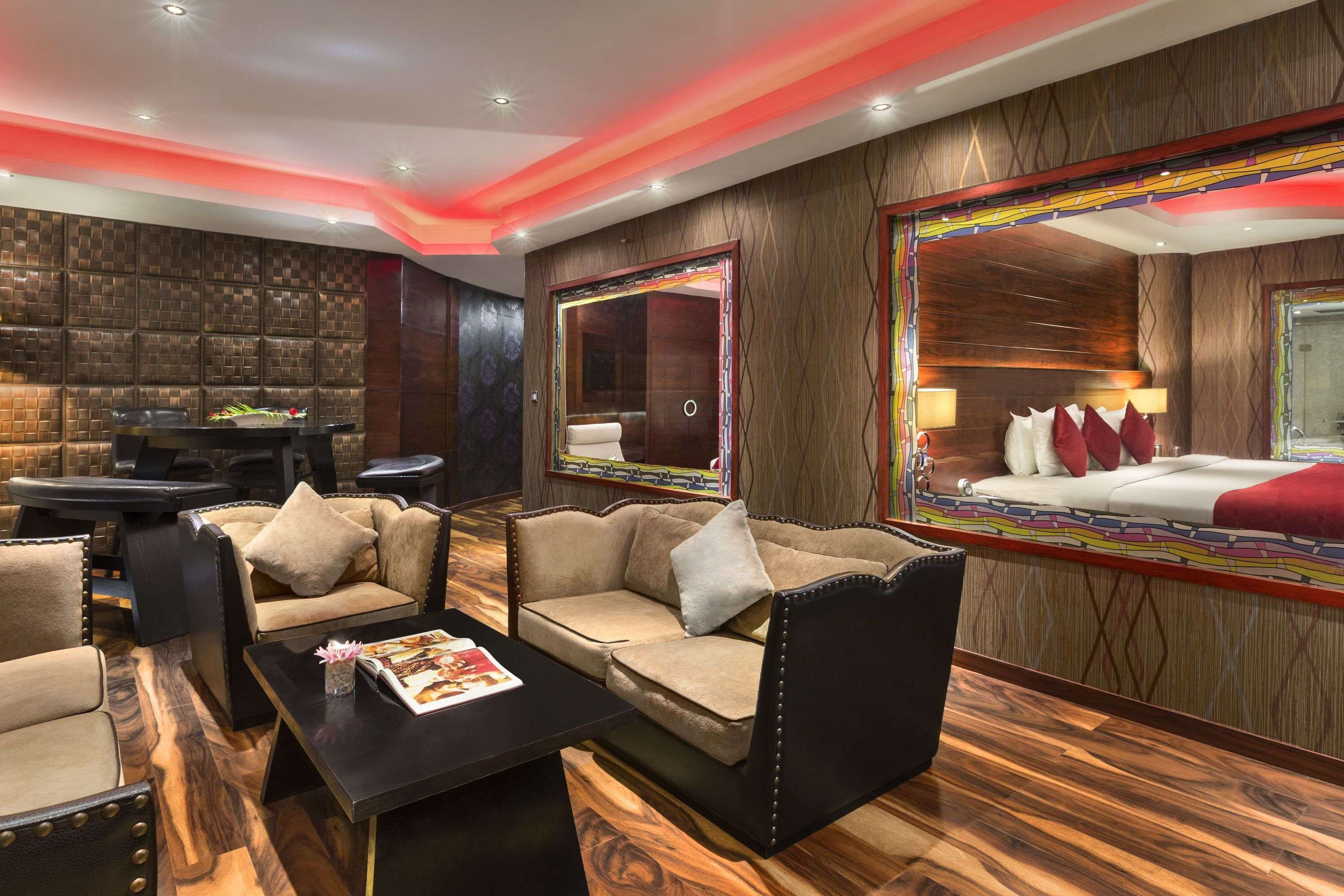 Ein modernes Hotelzimmer mit einer Couch, Sesseln, einem Couchtisch und einem großen Spiegel, der das Bett reflektiert.
