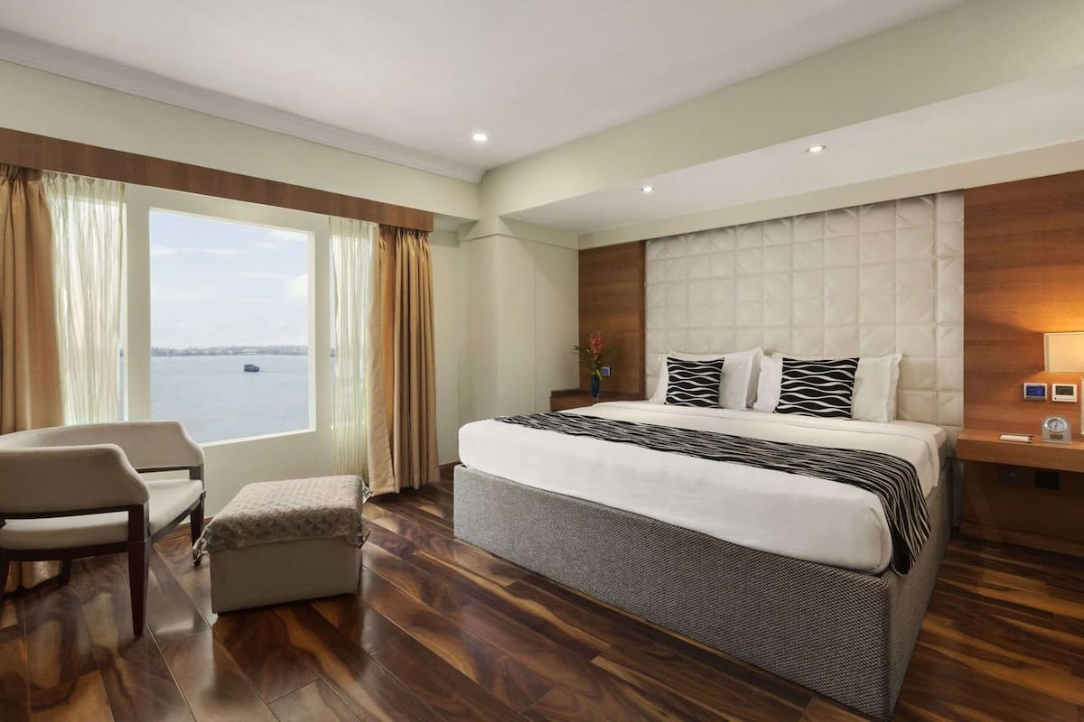 A hotel room with a large bed, a chair, a small table, and a view of the water.