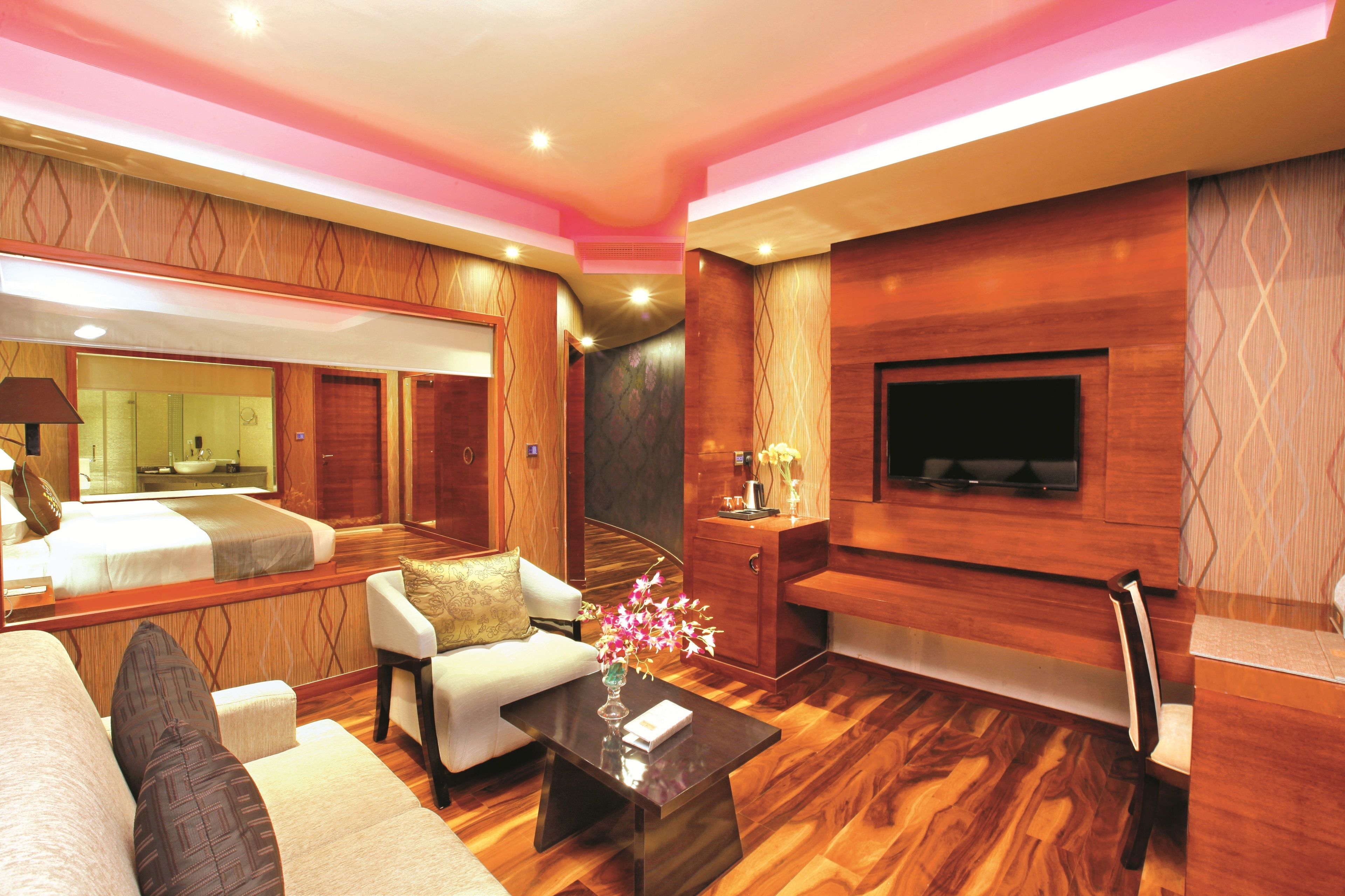 A modern hotel room with a large bed, a sofa, a coffee table, a TV, and a fireplace.