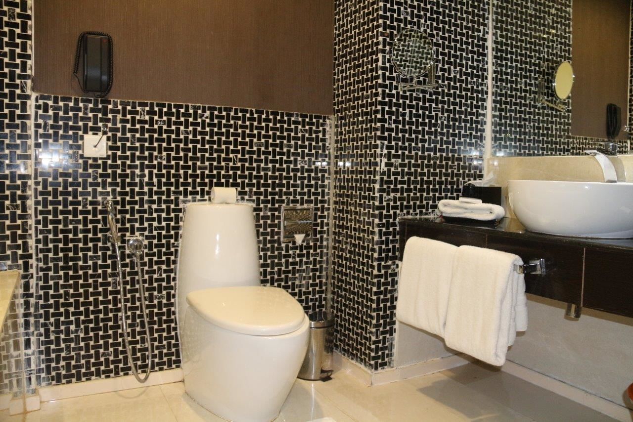 Une salle de bain avec un mur recouvert de carreaux aux motifs noir et blanc, des toilettes, un lavabo avec un grand miroir et un porte-serviettes.