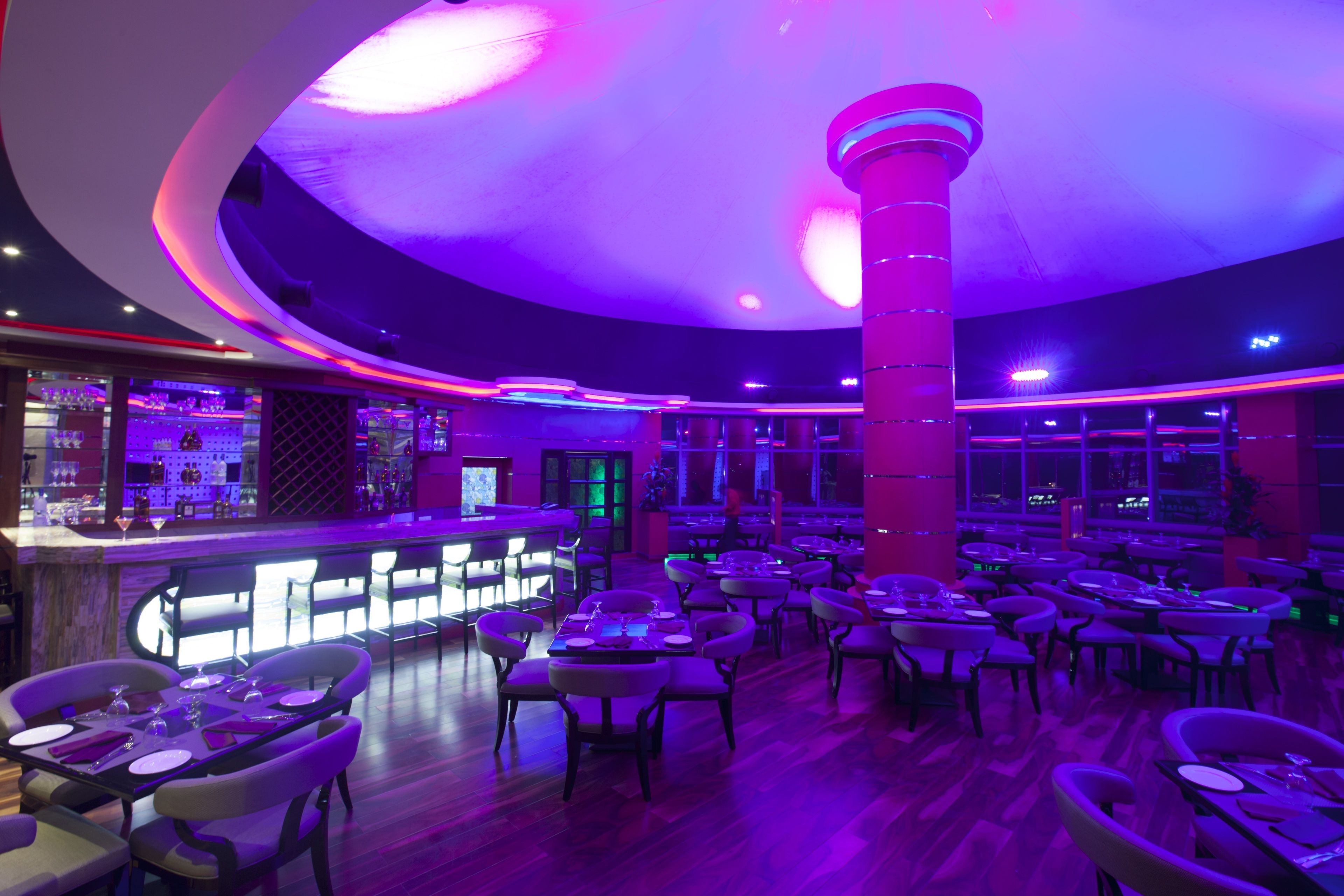 A restaurant with multiple tables and chairs, a bar area, and a distinctive ceiling design.
