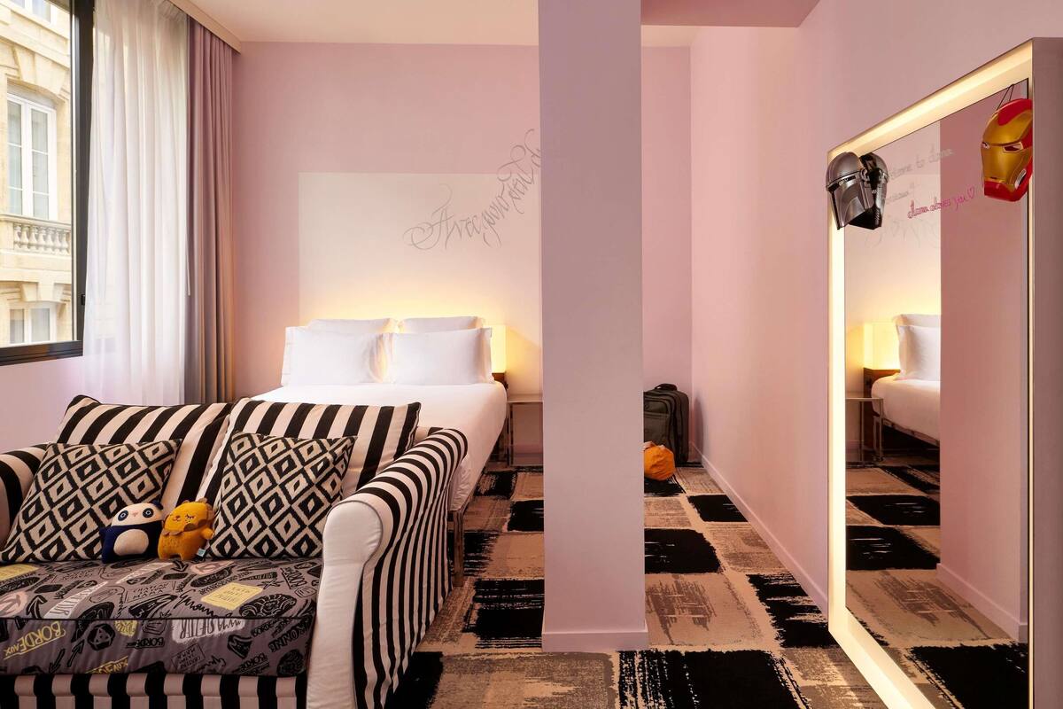 Een hotelkamer met een bed, een bank met gestreepte kussens, een spiegel en een raam met gordijnen.