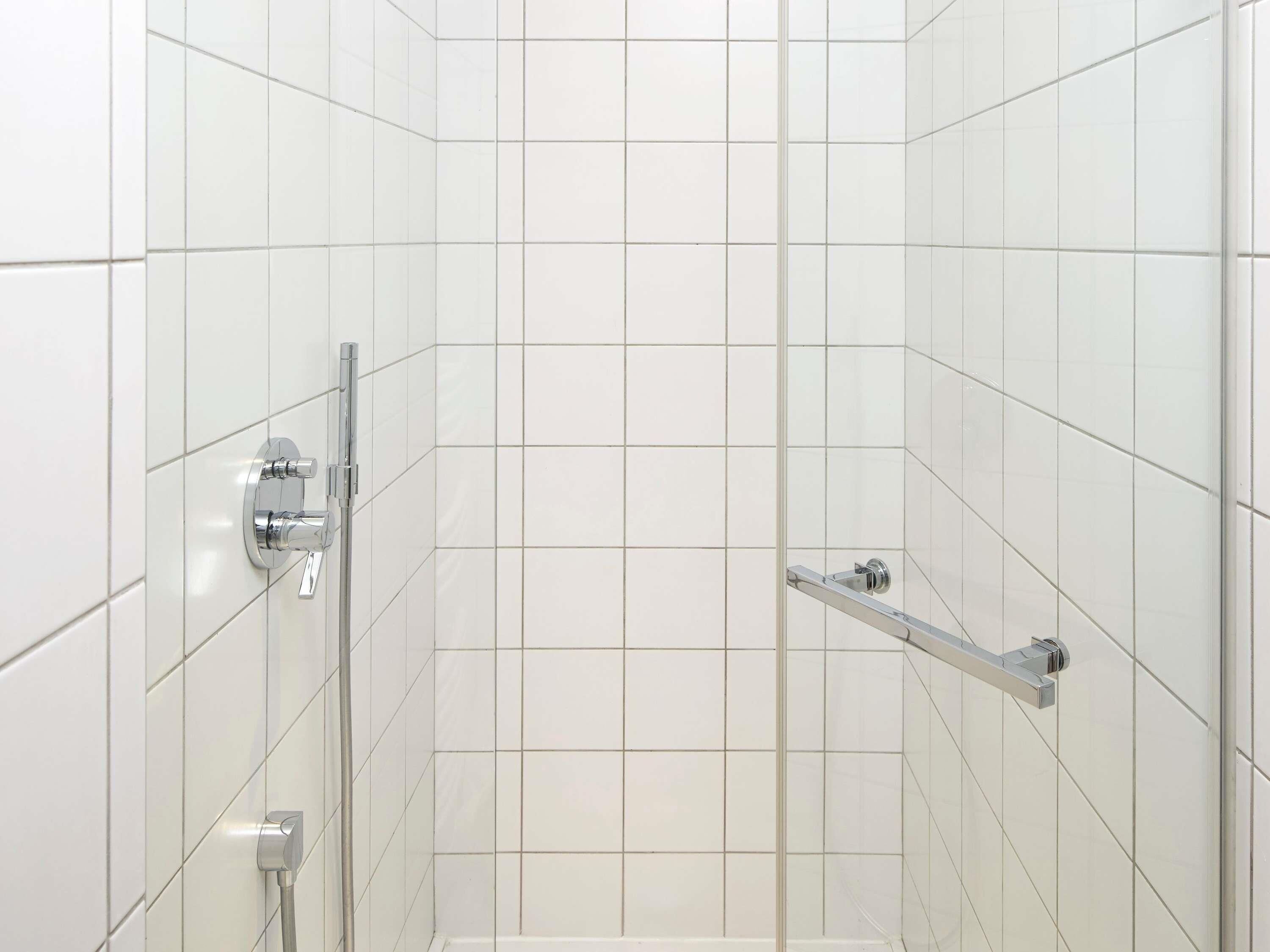 Ducha con azulejos blancos, cabezal de ducha cromado y ducha de mano.