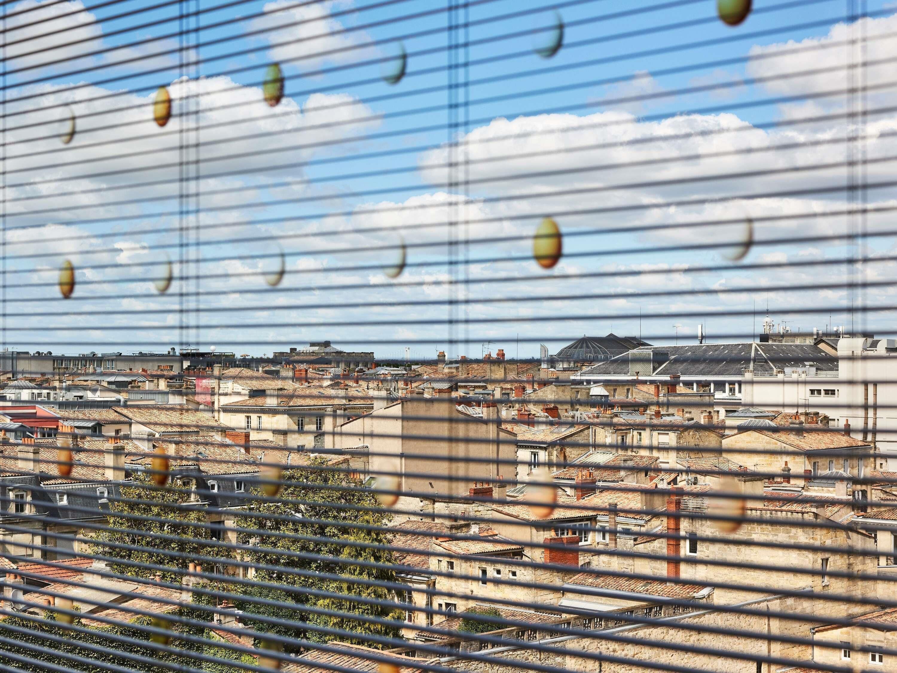 A cityscape viewed through window blinds with a view of rooftops and buildings.