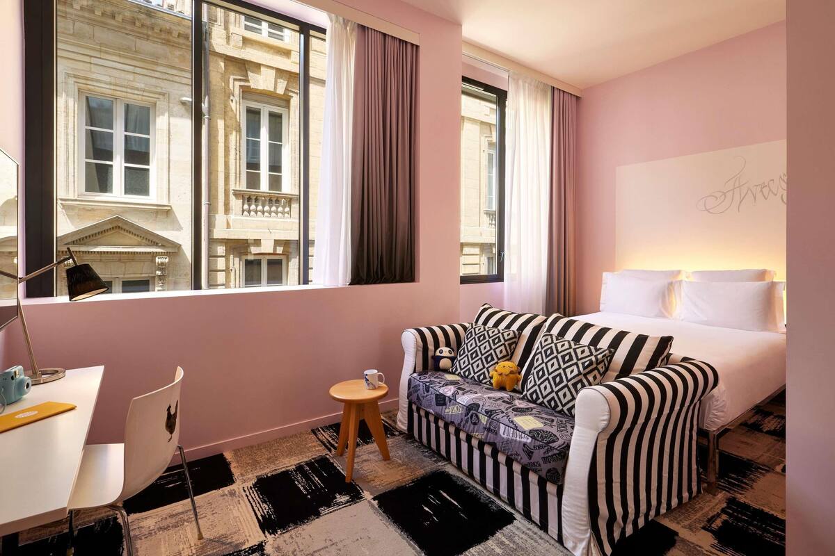 Een hotelkamer met een groot raam, een bed, een bank, een bureau en een stoel.